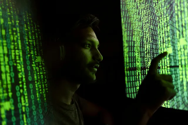 Homem observa códigos verdes projetados em telas digitais.