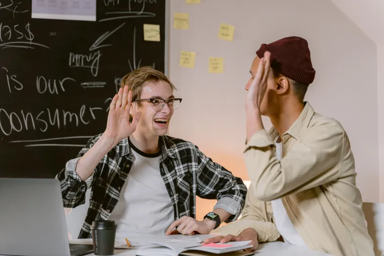Duas pessoas comemorando com toque de mãos em reunião de trabalho