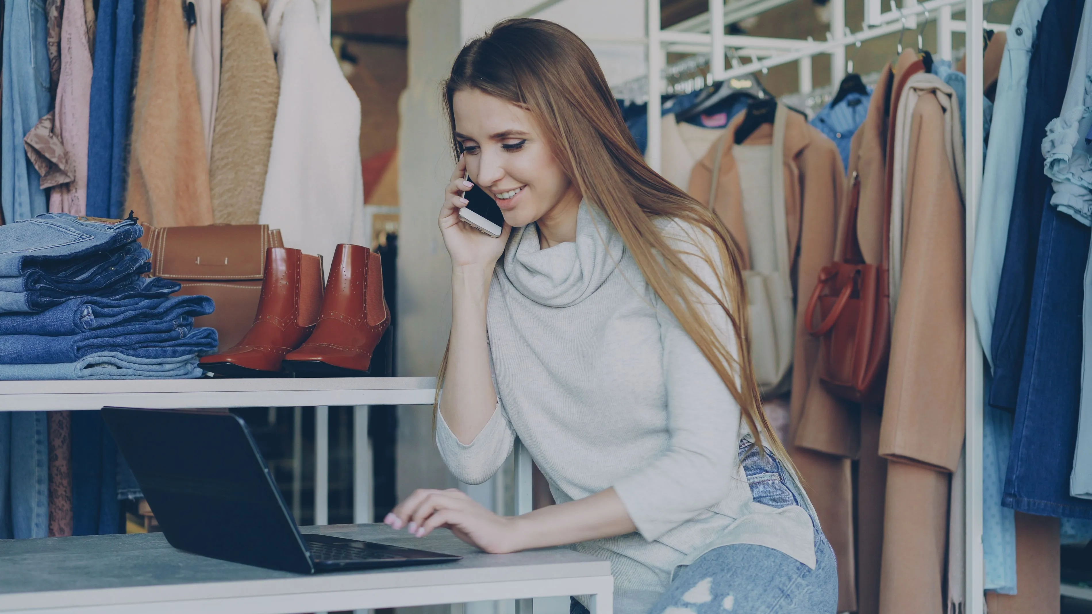 Mulher usando notebook e celular em loja de roupas e acessórios