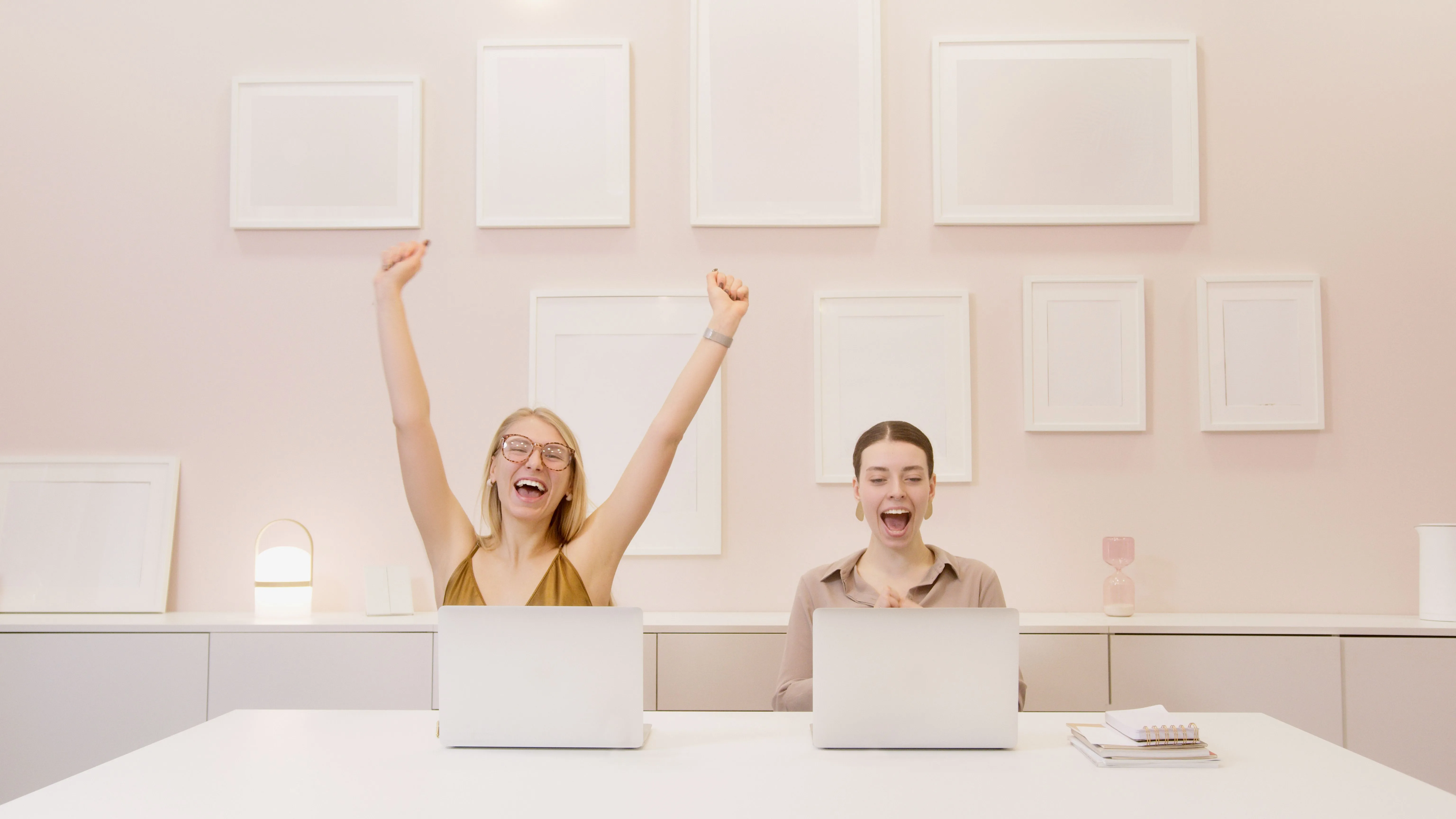 Duas mulheres comemoram diante de notebooks em um ambiente de trabalho.