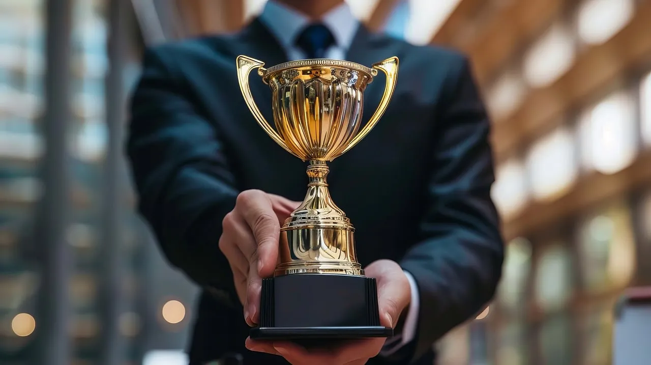 #FotoDescrição: Homem de terno segurando um troféu dourado, representando uma recompensa.