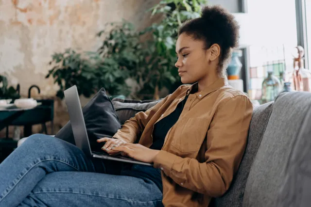 #FotoDescrição: Mulher sentada no sofá, concentrada no notebook, representando análise de dados e estratégias de marketing digital.