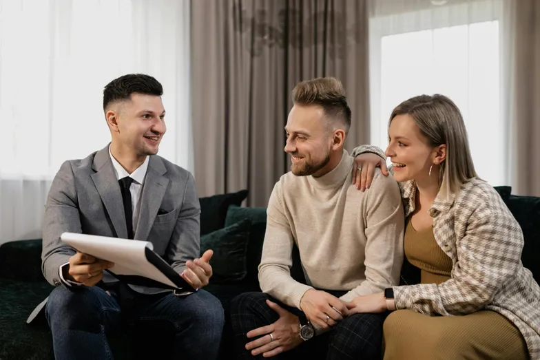 Casal em consulta imobiliária com consultor, avaliando imóveis em ambiente acolhedor.