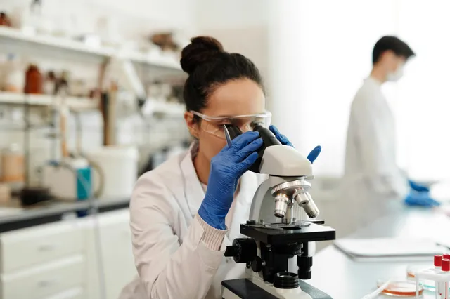Cientista observa amostra em microscópio dentro de laboratório.
