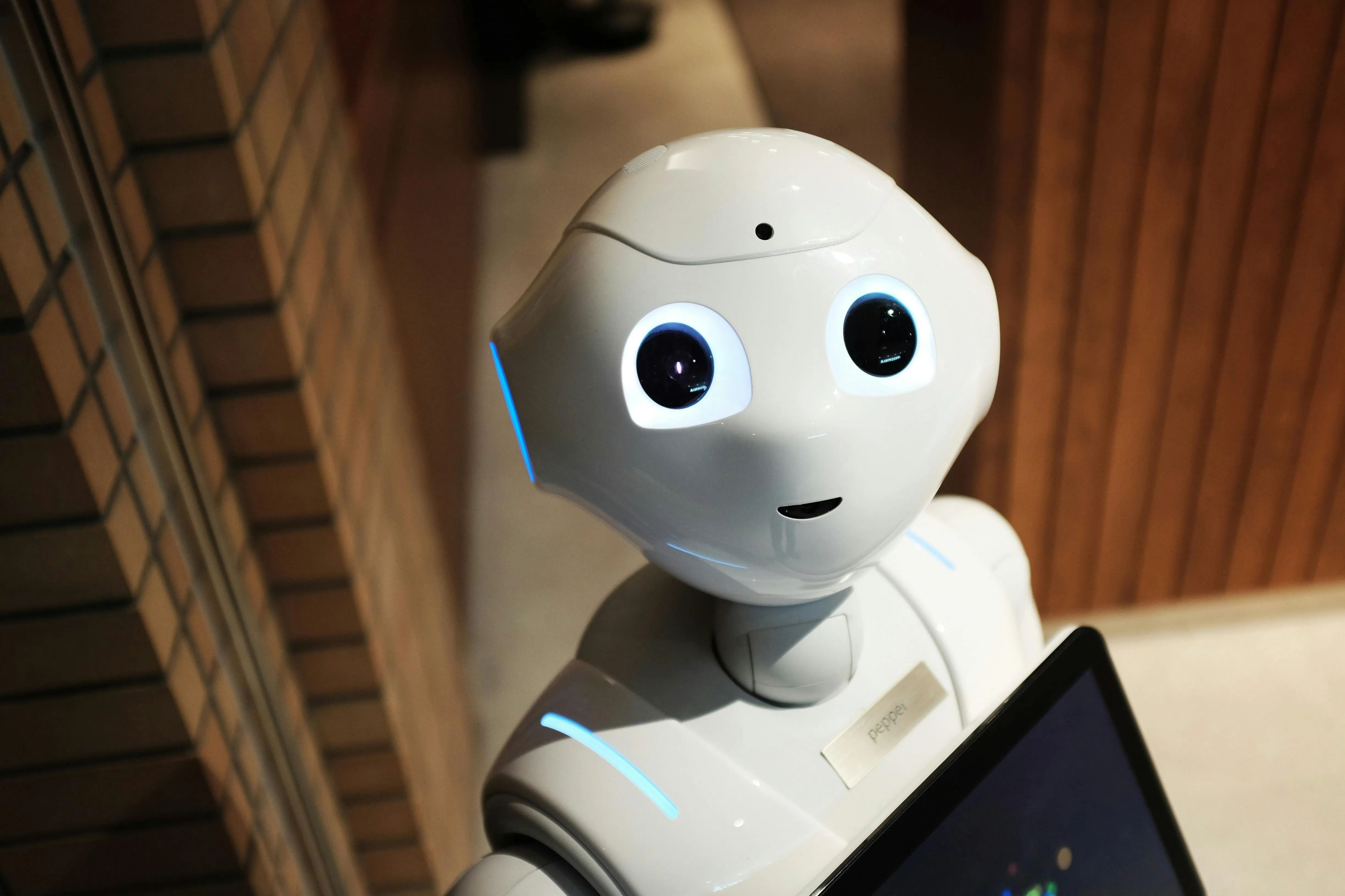 Robô amigável de olhos grandes interage com dispositivo em ambiente acolhedor.
