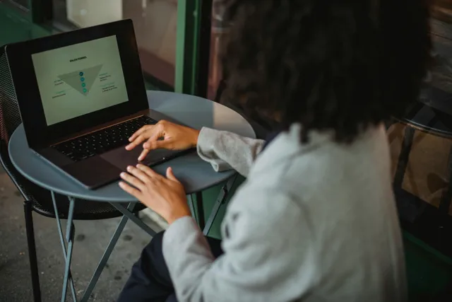 #FotoDescrição: Pessoa usando laptop em uma mesa redonda ao ar livre, analisando um funil de vendas exibido na tela.