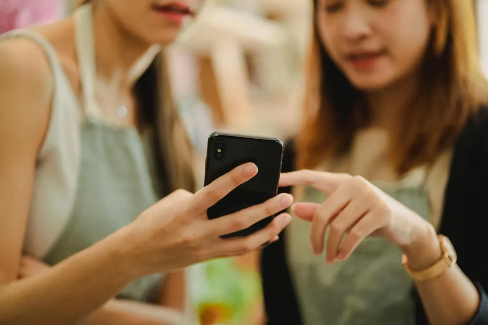 Duas pessoas olhando e apontando para a tela de um celular.