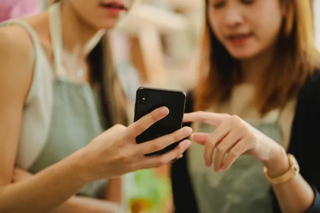 Duas pessoas olhando e apontando para a tela de um celular.