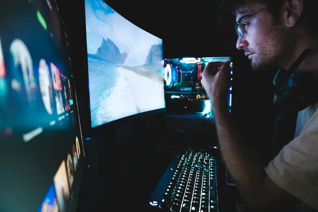 Homem usa computador com dois monitores em ambiente escuro.