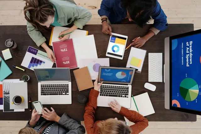 Equipe de negócios analisando gráficos e dados em laptops e tablets em escritório moderno.