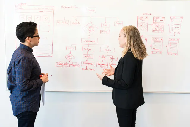 Dois colegas planejando um projeto em um quadro branco com diagramas