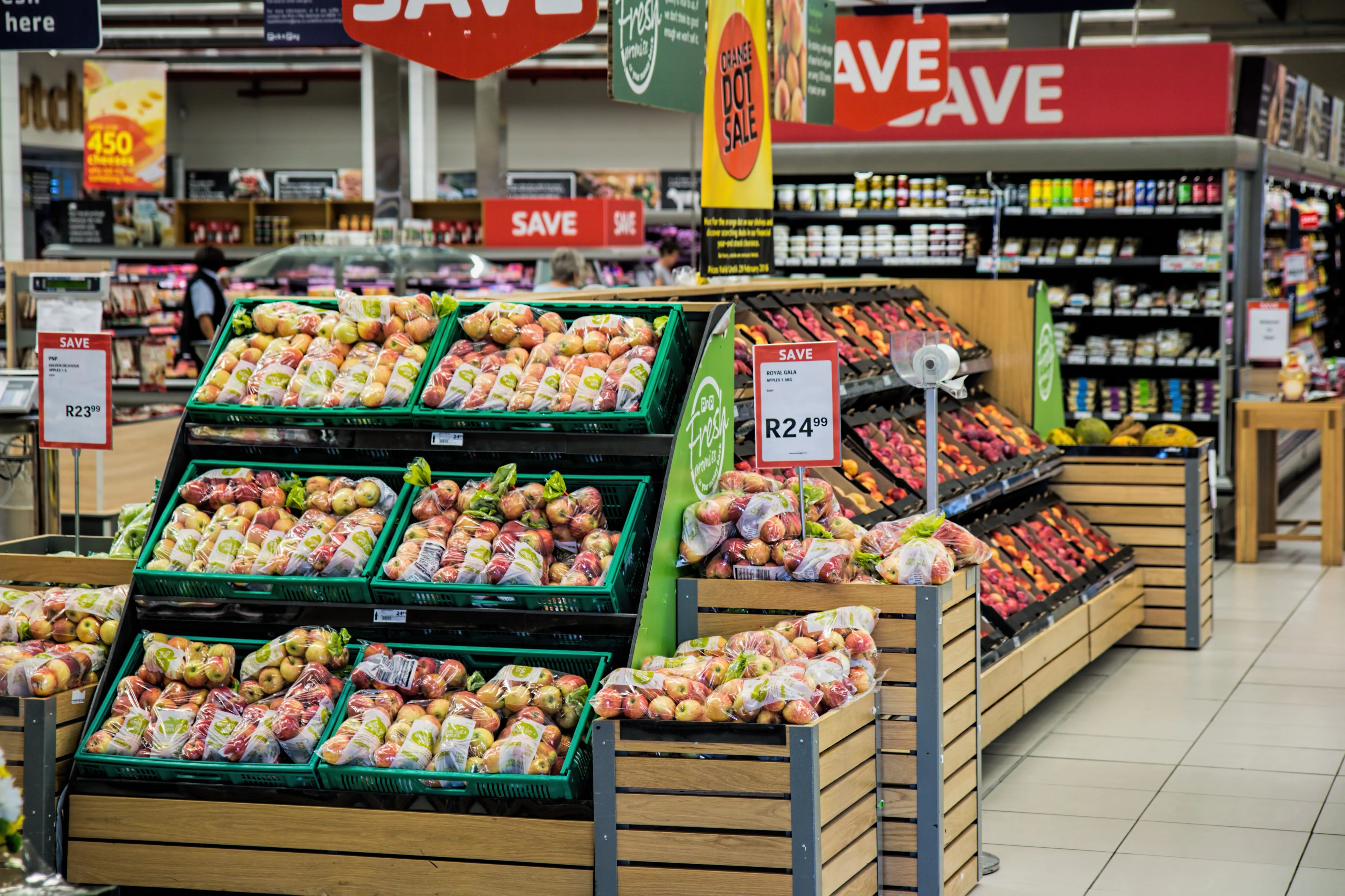 Expositor de frutas com maçãs e promoções em supermercado.