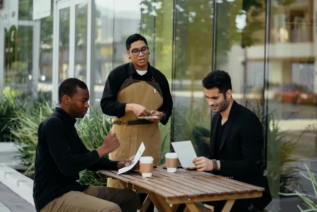 Amigos conversam e analisam pedidos em café ao ar livre.