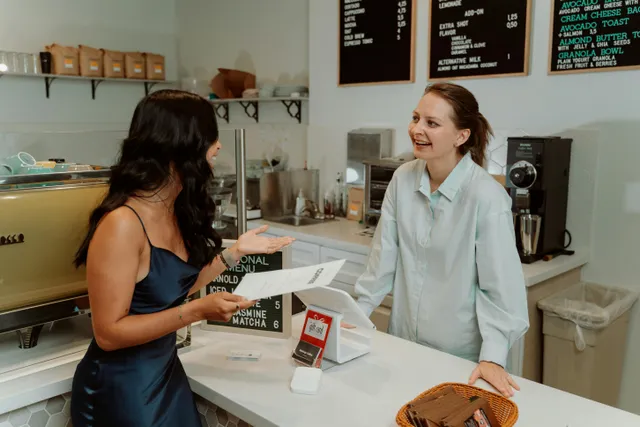Cliente conversa com atendente em café olhando cardápio e sorrindo