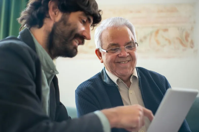 Dois homens sorrindo enquanto veem algo em um tablet.