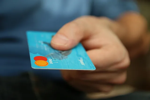 Mão segura cartão de débito azul para pagamento.