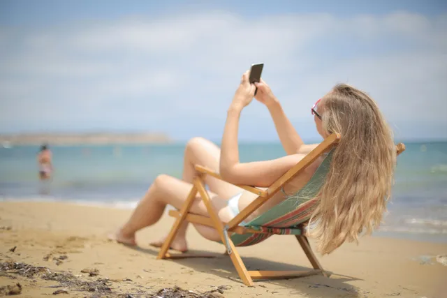 Mulher relaxando em cadeira de praia usando celular à beira-mar