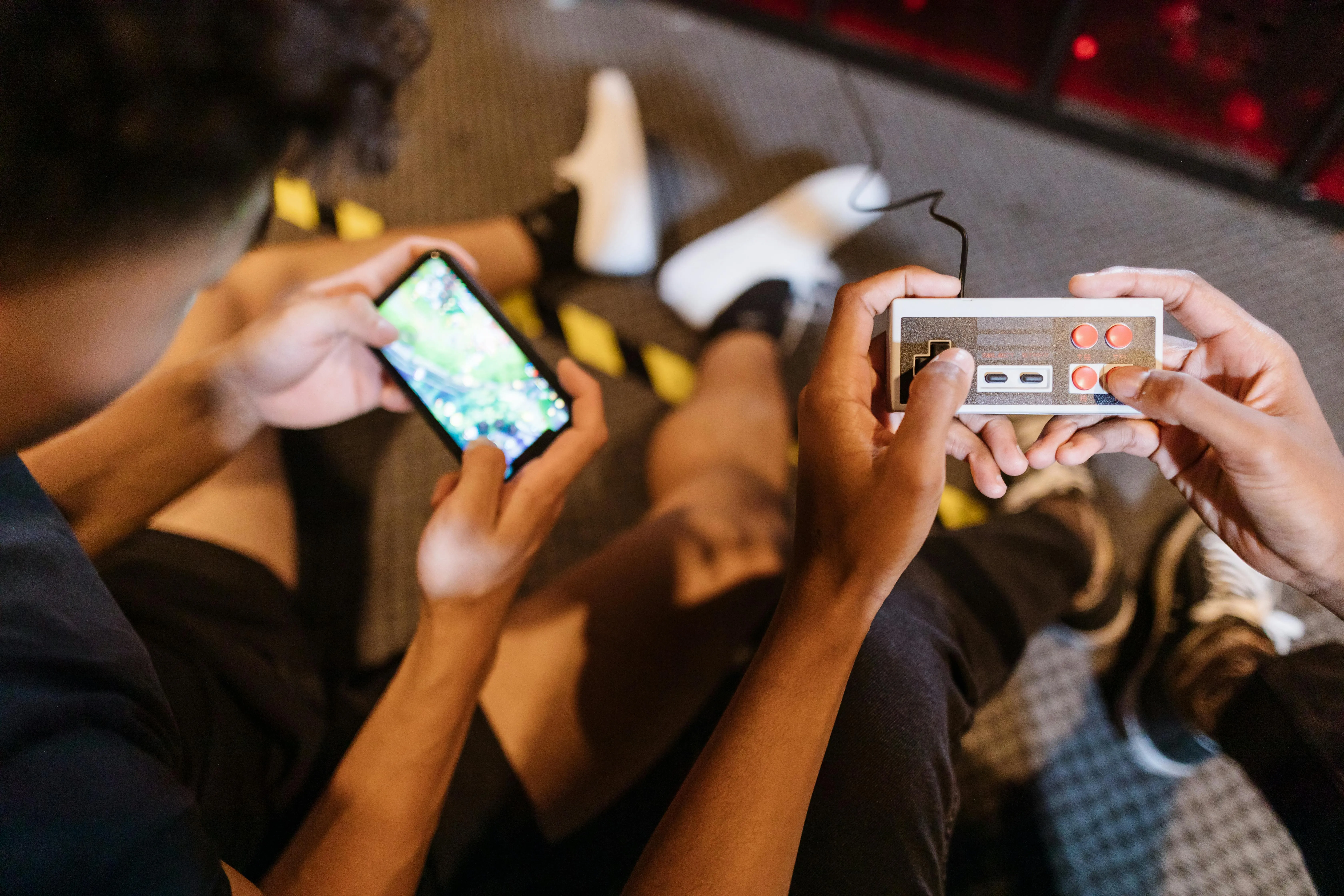 #FotoDescrição: Pessoas jogando juntos, uma segurando um controle retrô e outra com smartphone.