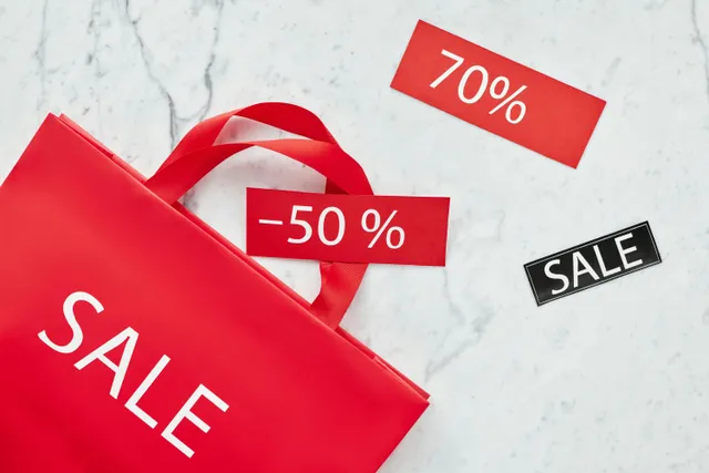 Sacola vermelha com etiquetas de desconto e palavra “SALE” sobre mesa