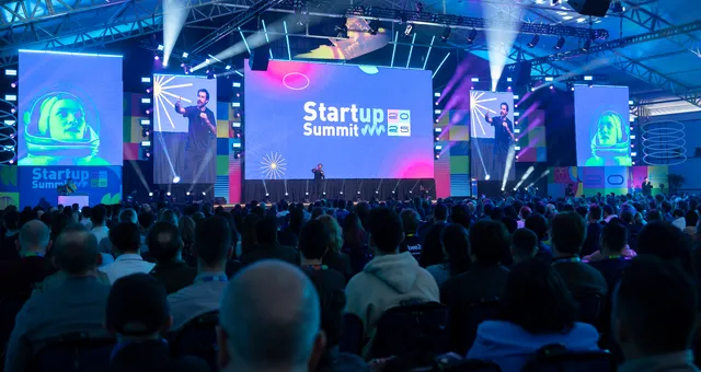 #FotoDescrição: Auditório cheio no Startup Summit 2025 com palco iluminado.