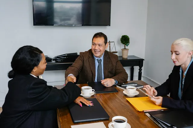 Pessoas em reunião de negócios apertam as mãos em mesa com café e documentos