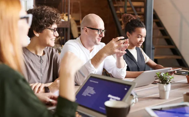 Grupo em reunião descontraída com notebooks e tablets sobre a mesa.