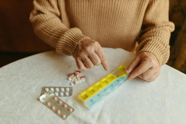 #FotoDescrição: Uma pessoa organizando medicamentos em um organizador semanal de comprimidos, representando a importância da adesão ao tratamento.